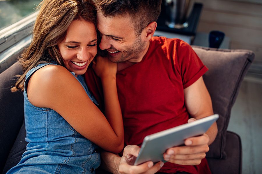 Client Center - Closeup View of Young Smiling Couple Sitting at Home Using a Tablet