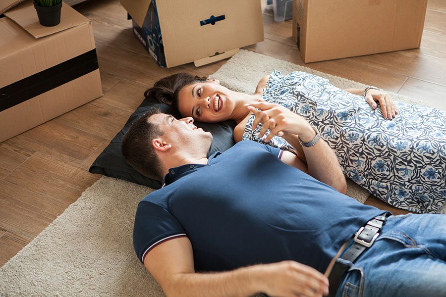 Personal Insurance - View of Cheerful Young Couple Laying on the Floor in the Living Room Next to Their Moving Boxes as They Celebrate Their New Home